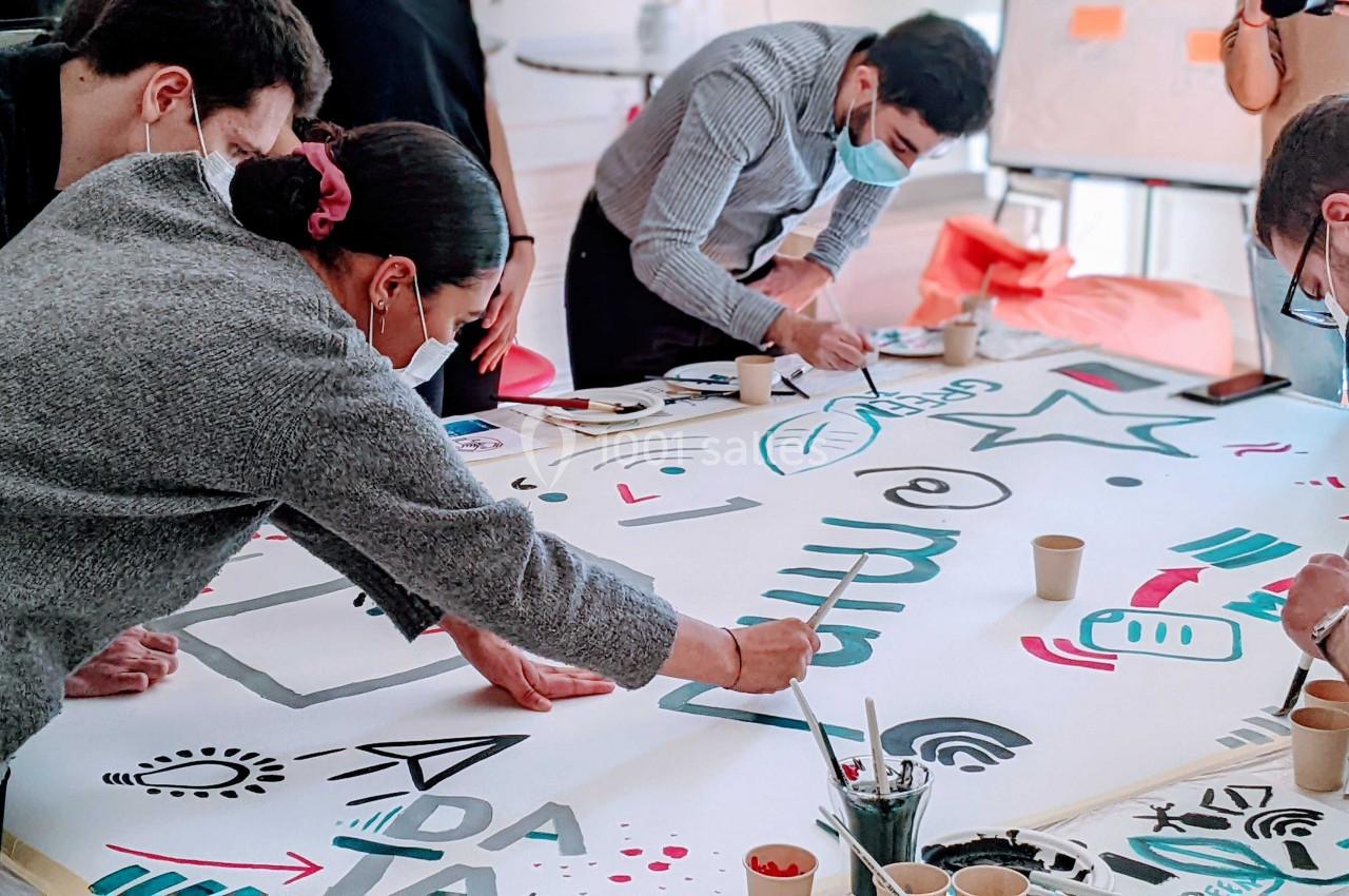 Des personnes collaborent autour d'une grande table, dessinant et écrivant sur une affiche blanche.