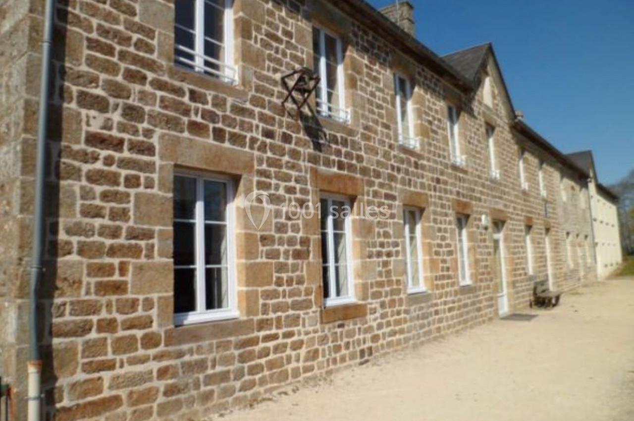Façade en pierre d'une maison traditionnelle avec plusieurs fenêtres blanches, sous un ciel bleu clair.