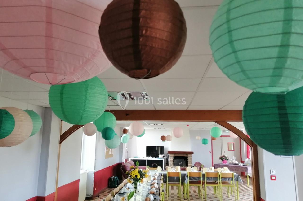 Salle décorée avec des lanternes en papier colorées suspendues au plafond, tables dressées pour un repas festif.