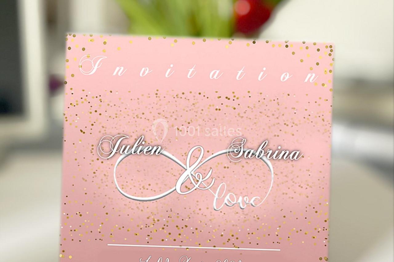 Carte d'invitation rose avec des motifs dorés, portant les prénoms ’Julien et Sabrina’ et une date en bas.
