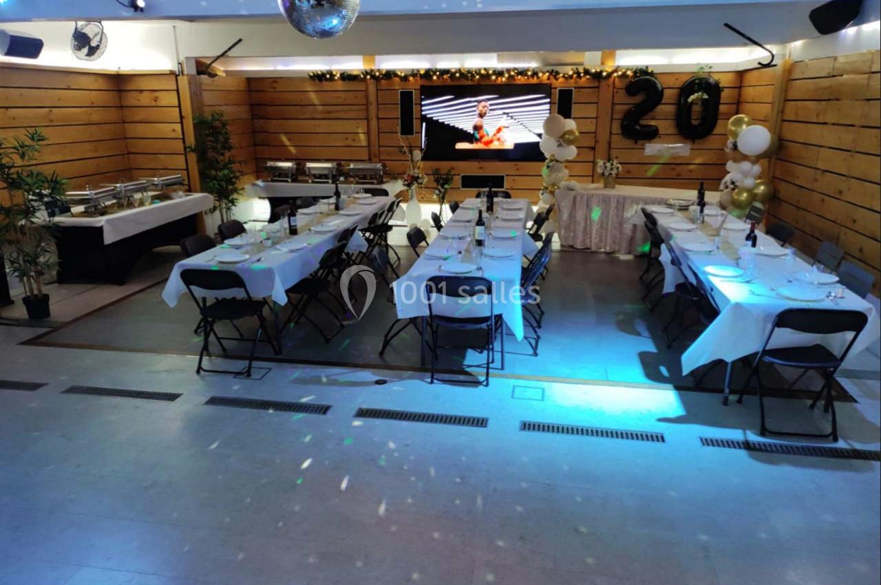 Salle décorée pour une fête avec tables dressées, ballons dorés et blancs, et écran en arrière-plan.