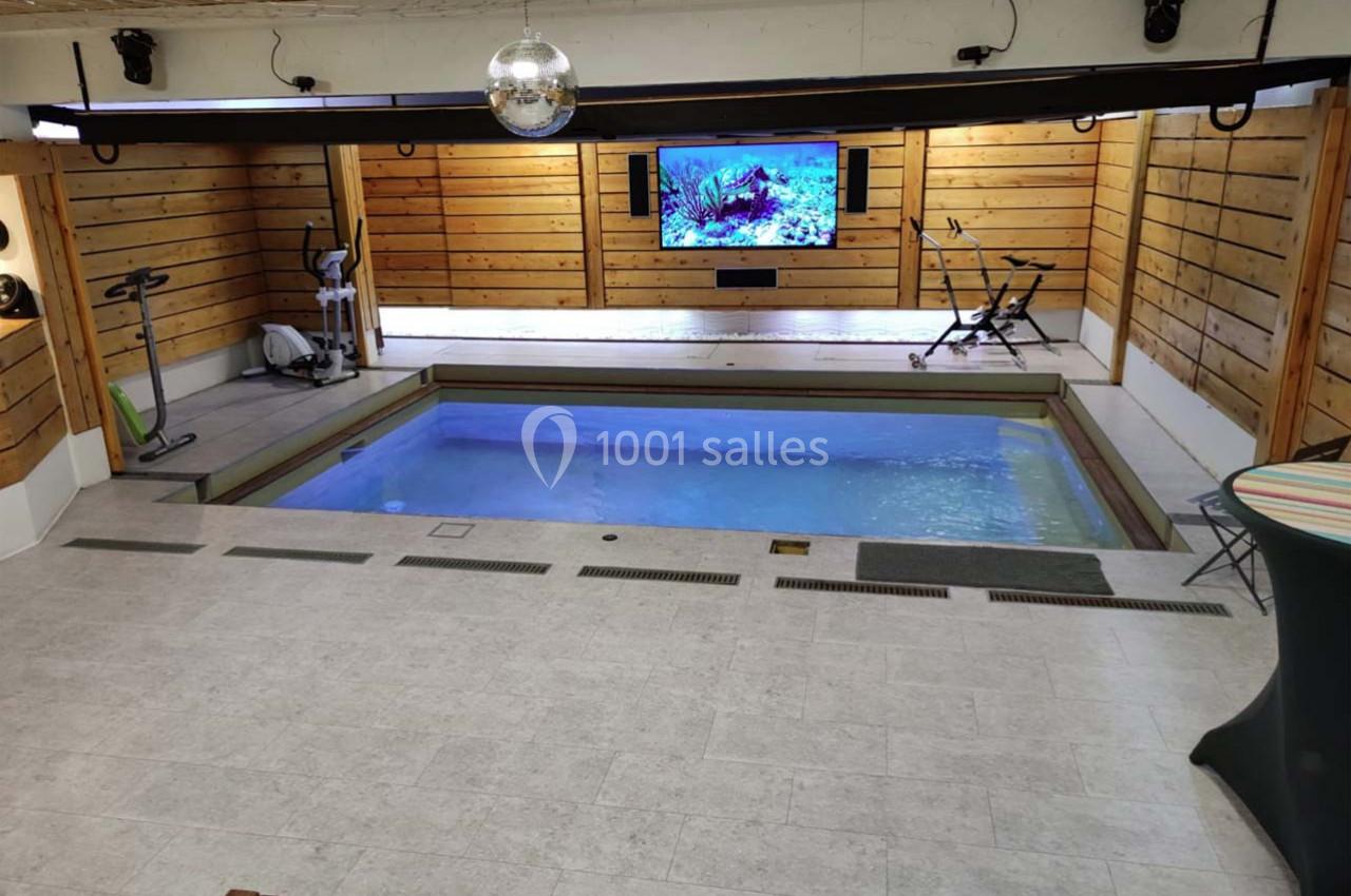 Salle intérieure avec piscine, équipements de sport, murs en bois et écran affichant une image sous-marine.