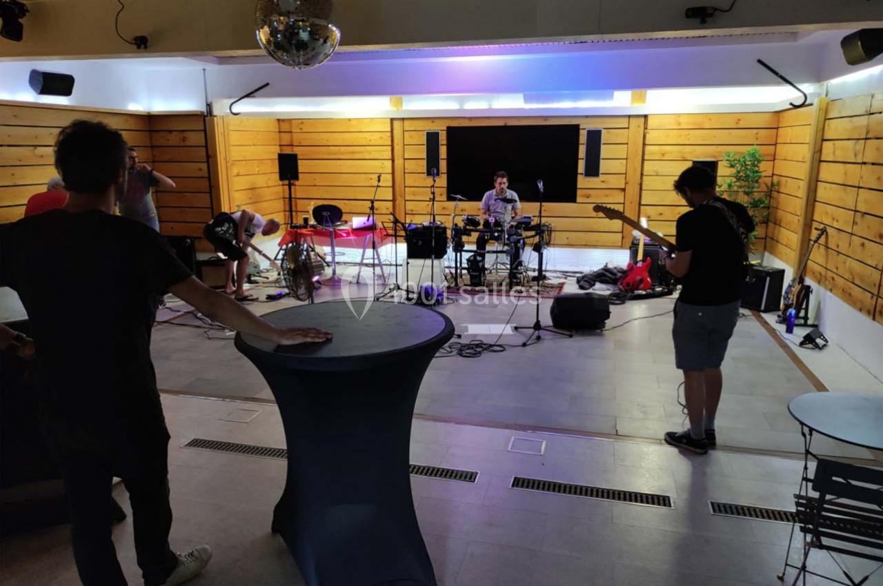 Un groupe de musiciens répète dans une salle équipée de panneaux en bois, avec instruments et matériel sonore.