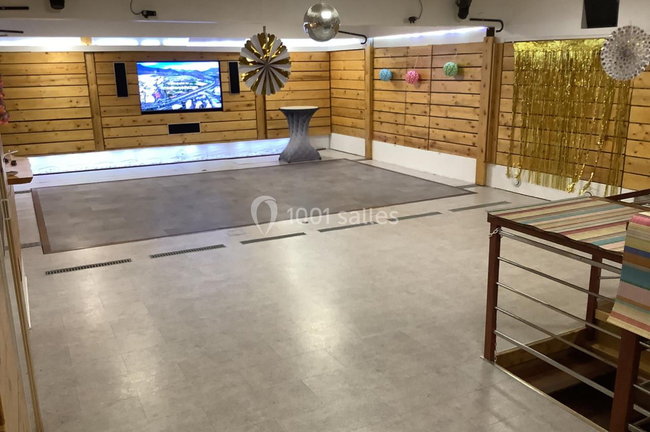Salle vide avec parquet, murs en bois, décorations suspendues et écran mural allumé.