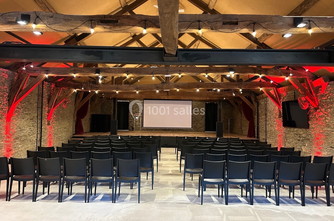 Salle de conférence avec des rangées de chaises noires, un écran de projection et des murs en pierre éclairés.