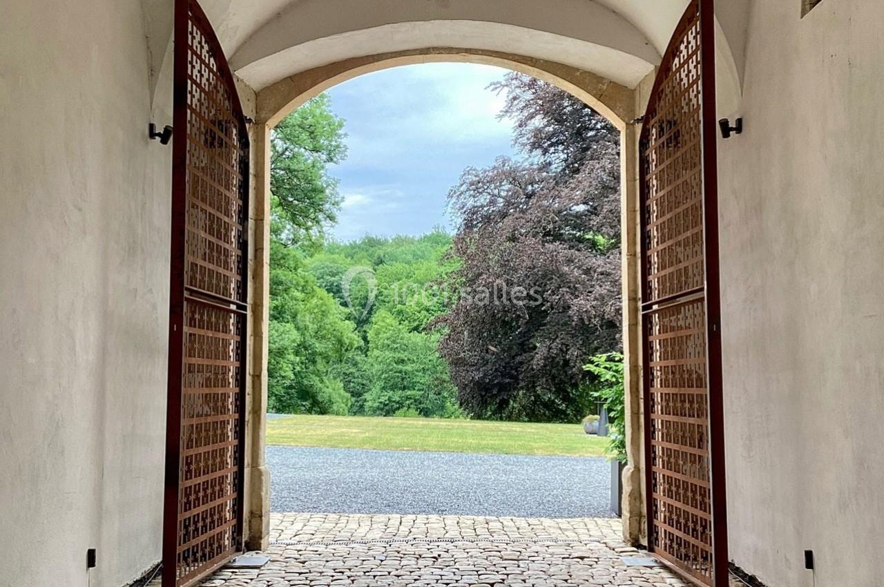 Vue d'une allée pavée traversant une arche ouverte, donnant sur un jardin verdoyant et des arbres.