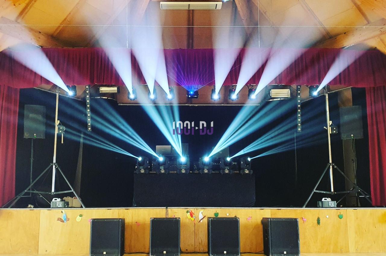 Scène de spectacle avec projecteurs lumineux, enceintes et équipement de DJ installé sous un rideau rouge.