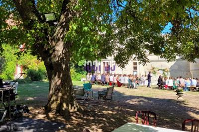 Salle de réception en pierre avec invités assis et debout, décorations florales suspendues et ambiance chaleureuse.