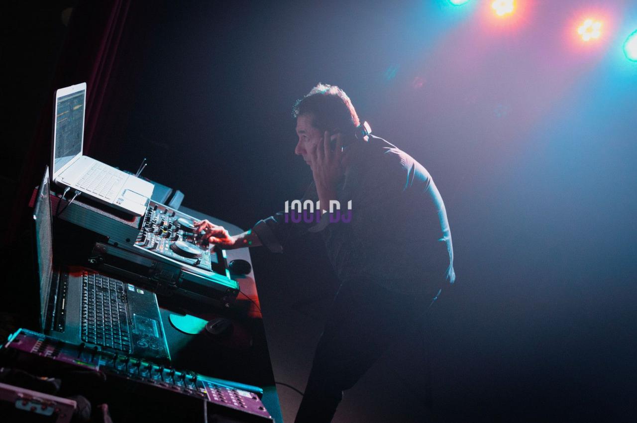 Un DJ mixe de la musique sur une table de mixage éclairée par des lumières colorées dans une ambiance sombre.