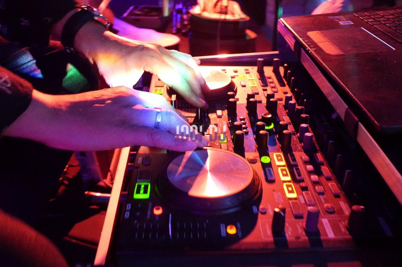 Mains manipulant une table de mixage audio éclairée par des lumières colorées dans un environnement sombre.