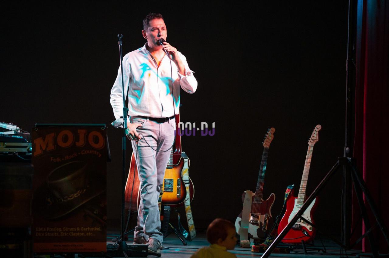 Un homme chante sur scène avec des guitares en arrière-plan et un éclairage de spectacle.