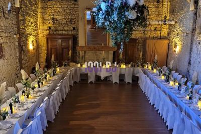 Salle de réception en pierre avec invités assis et debout, décorations florales suspendues et ambiance chaleureuse.
