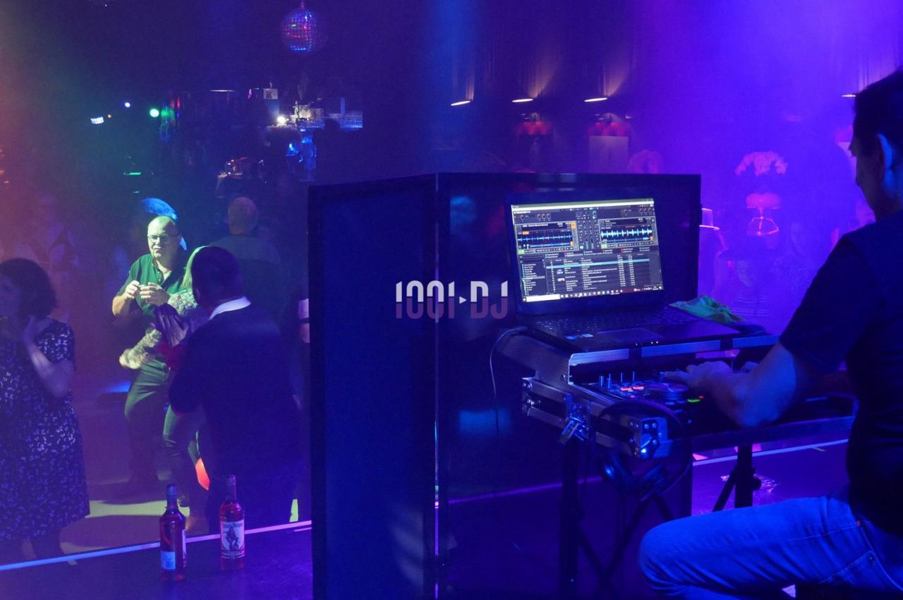 Un DJ mixe sur scène dans une boîte de nuit, avec des lumières colorées et des danseurs sur la piste.