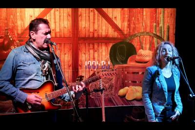 Salle de réception en pierre avec invités assis et debout, décorations florales suspendues et ambiance chaleureuse.