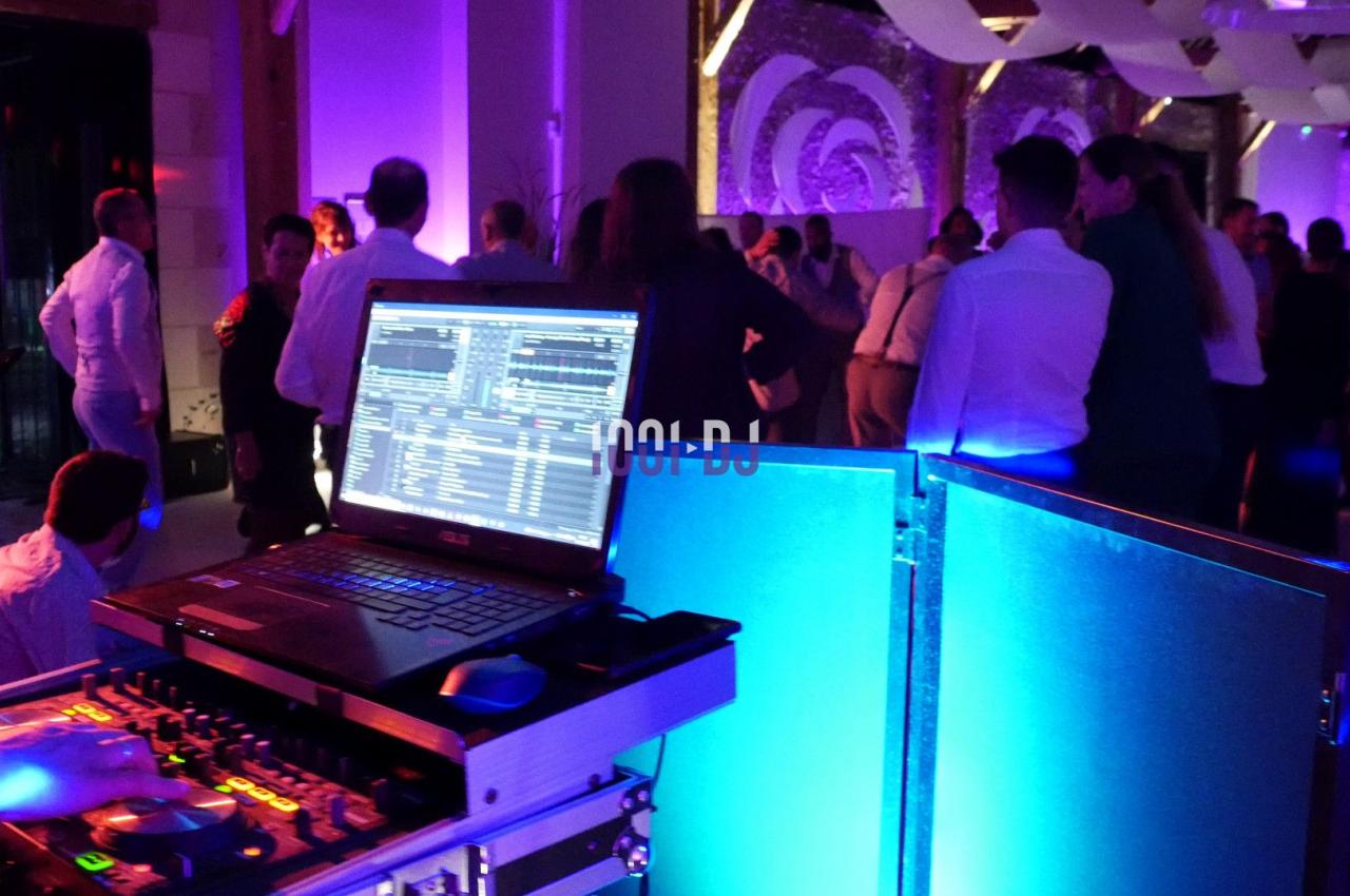 Un ordinateur portable avec une interface DJ en premier plan, des personnes dansant dans une salle éclairée en violet.