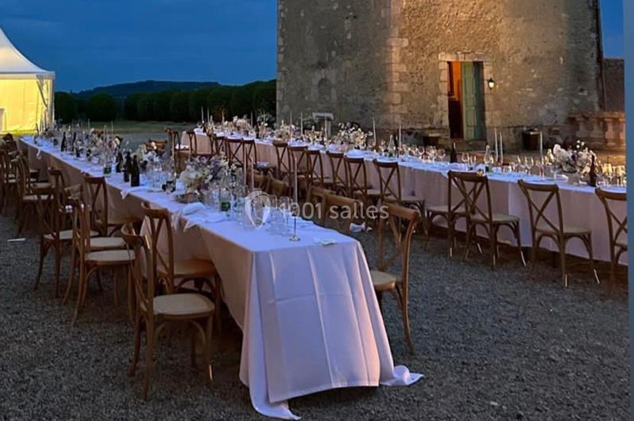 Tables longues dressées pour un dîner en extérieur, avec nappes blanches, chaises en bois et éclairage tamisé au crépuscule.