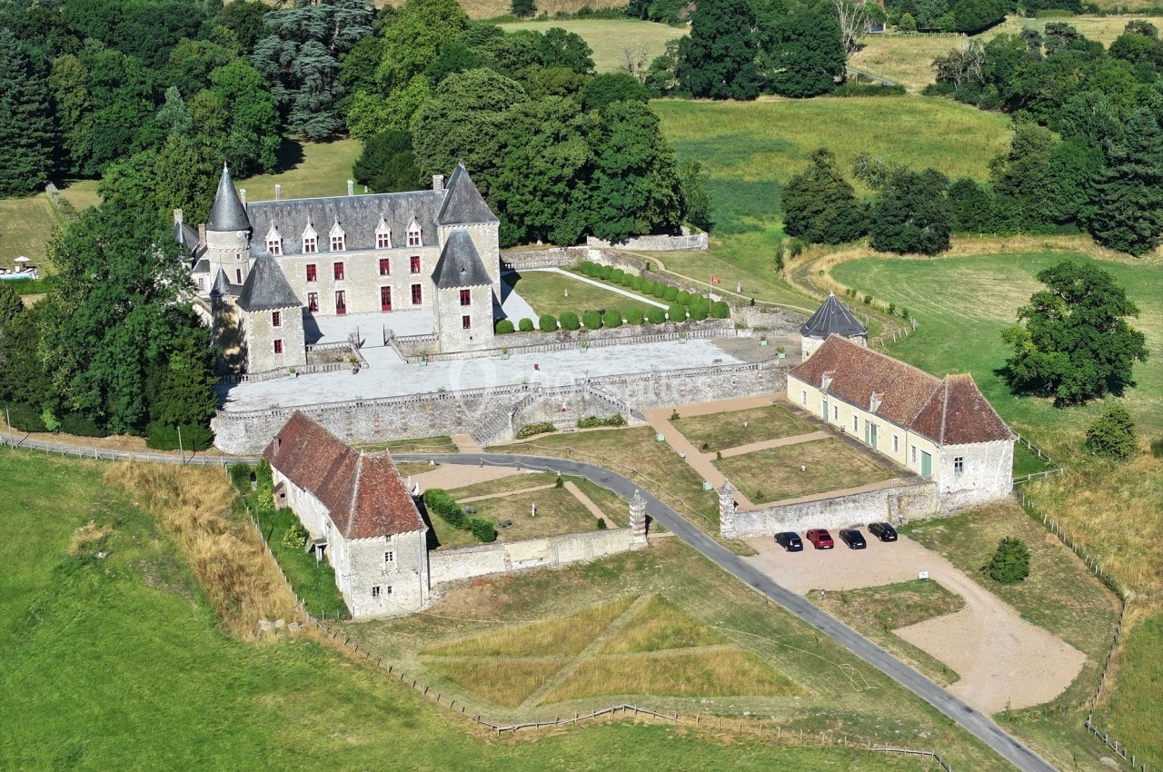 Vue aérienne d'un château historique entouré de bâtiments annexes, de jardins et de prairies verdoyantes.