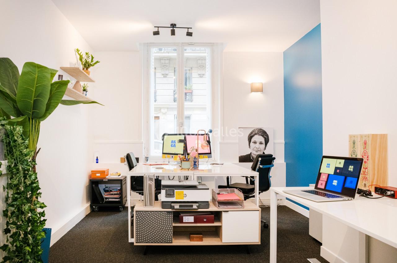 Bureau moderne avec mobilier blanc, plantes vertes, ordinateurs allumés et grande fenêtre laissant entrer la lumière…