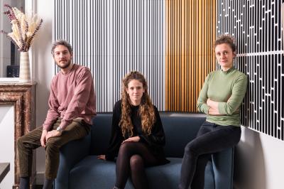 Miniature Arca Productions #4 Trois personnes assises et debout dans un intérieur moderne avec des panneaux muraux décoratifs en arrière-plan.