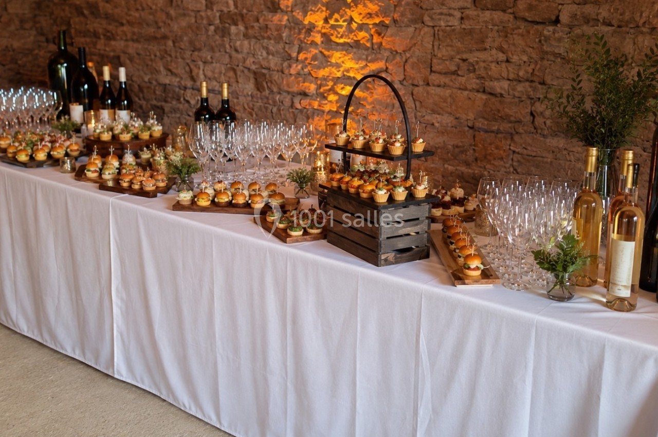 Table de réception avec verrines, bouteilles de vin et verres, disposée devant un mur en pierre éclairé.