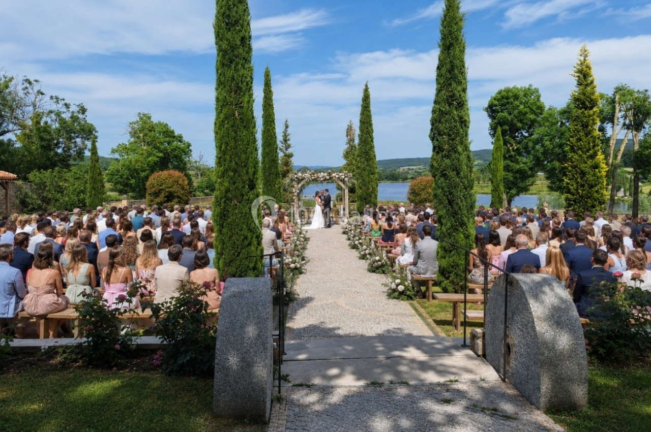 Cérémonie de mariage en plein air avec des invités assis, allée centrale bordée de cyprès et vue sur un paysage verdoyant.