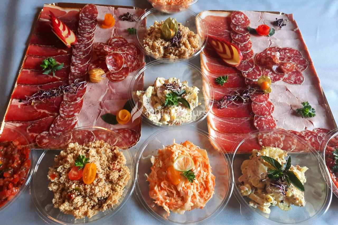 Plateau de charcuterie variée entouré de salades composées, présenté sur une table avec décoration soignée.
