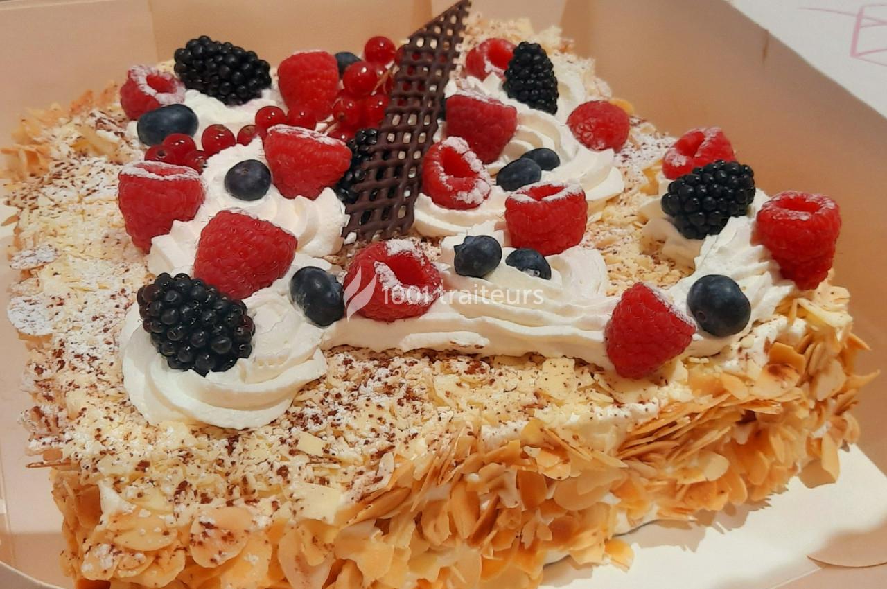 Gâteau rectangulaire décoré de fruits rouges, crème chantilly, copeaux d'amandes et une garniture en chocolat.