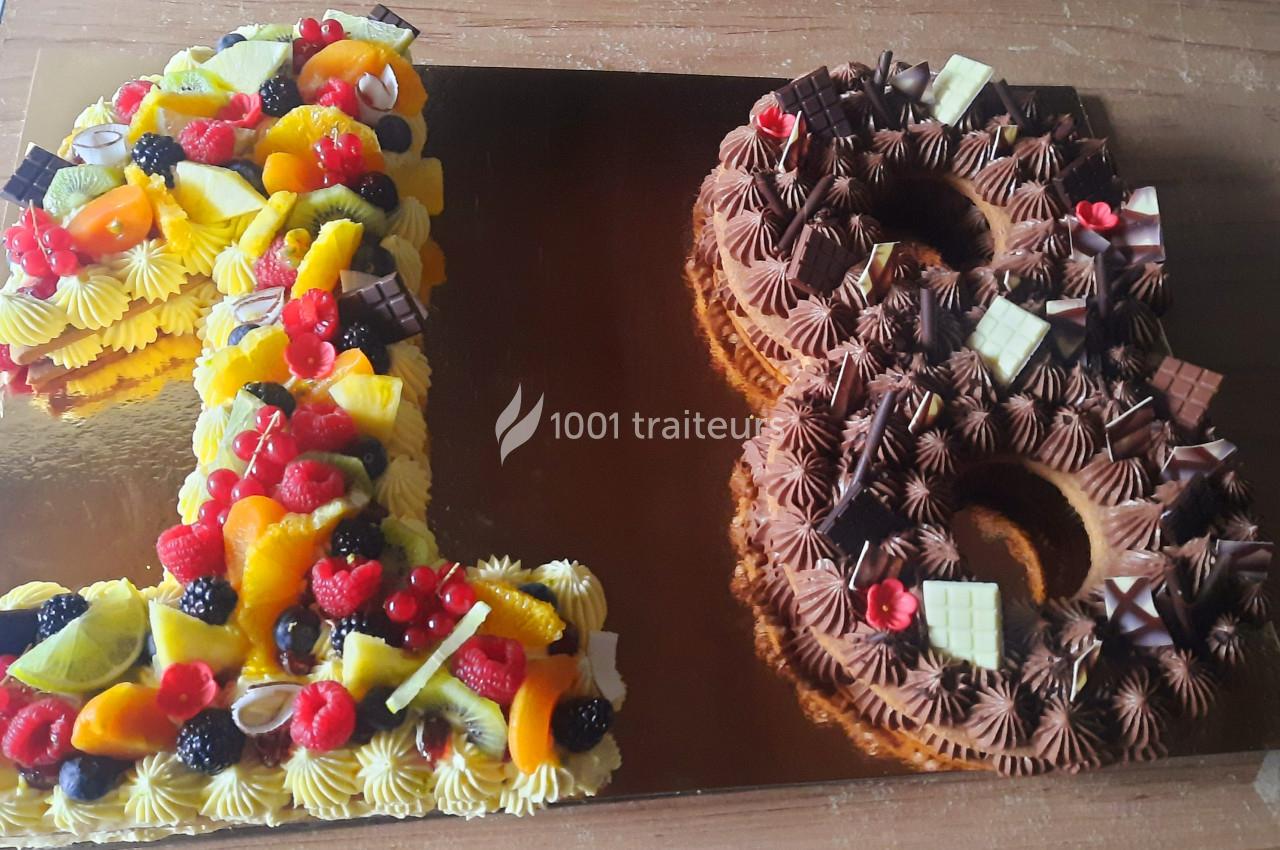 Gâteau en forme du chiffre 18, décoré de fruits frais, de chocolat et de crème colorée.