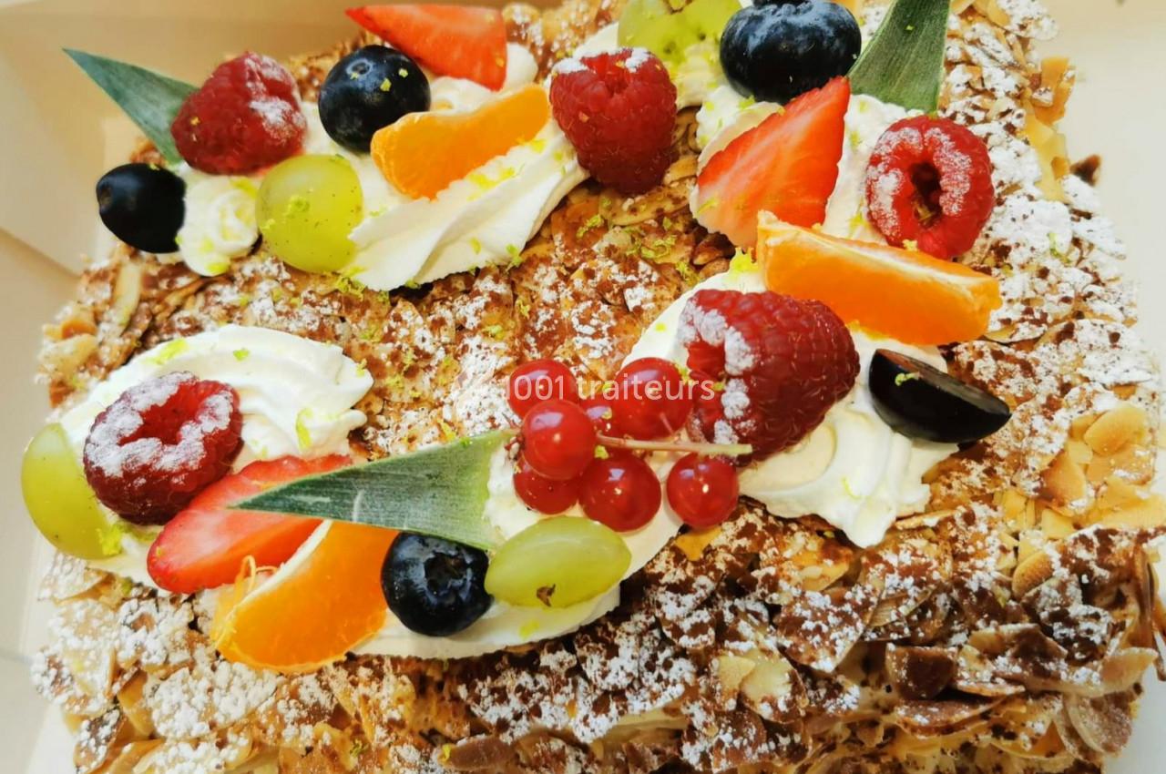 Gâteau décoré de fruits frais variés, crème chantilly et amandes effilées, saupoudré de sucre glace.