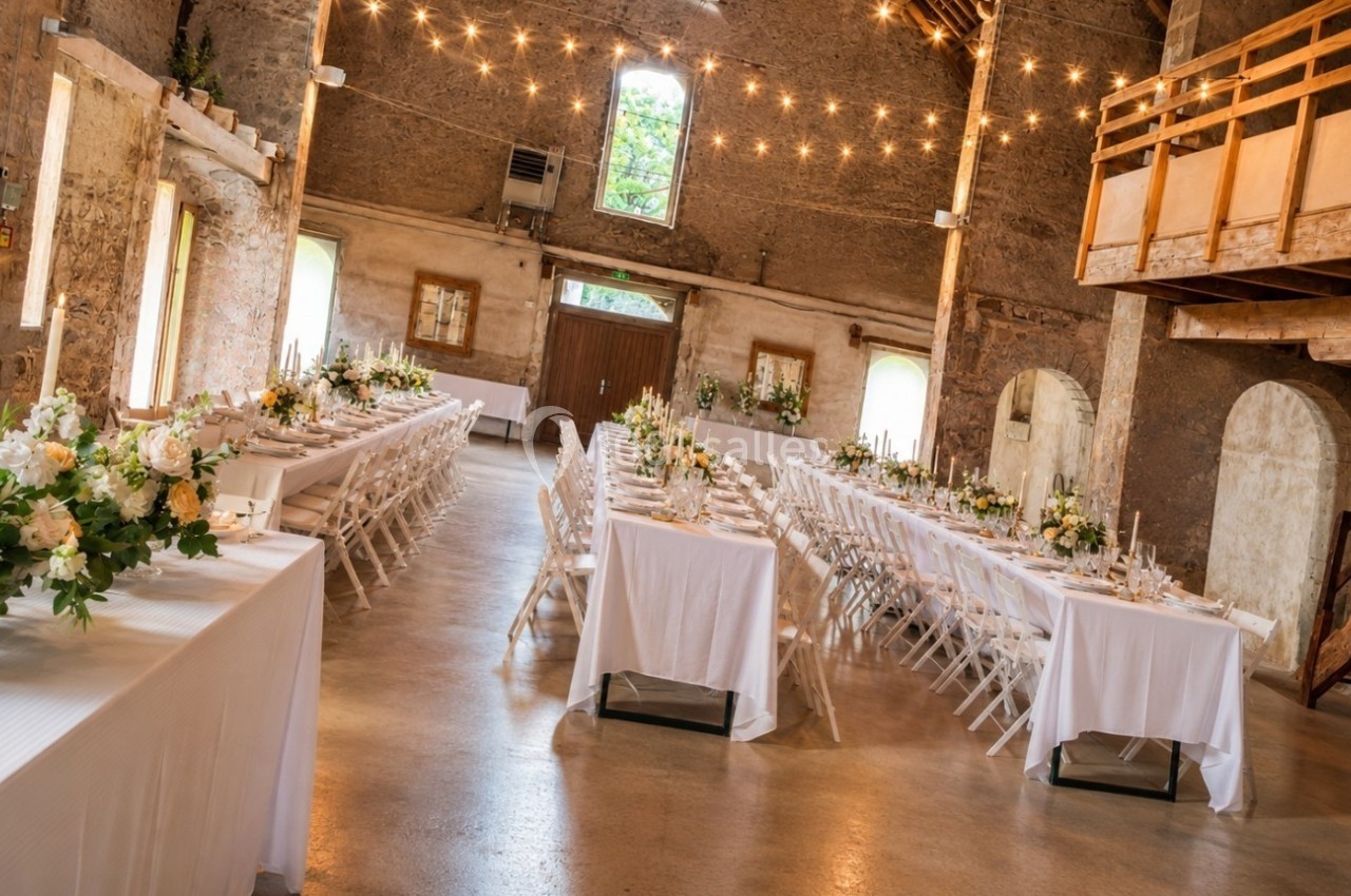 Salle de réception rustique décorée pour un mariage, avec longues tables blanches et arrangements floraux.