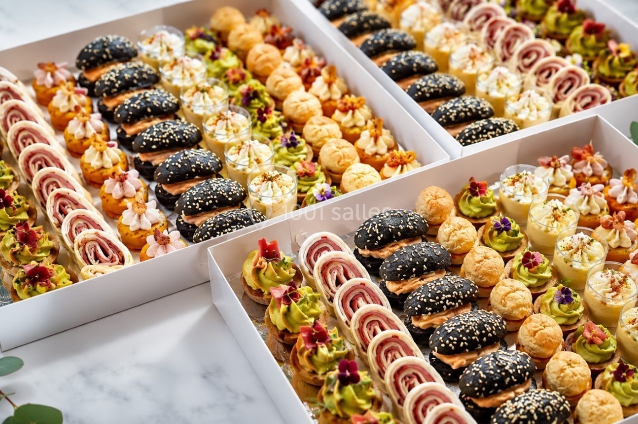Plateaux de bouchées apéritives variées comprenant mini-burgers, roulés, choux garnis et verrines sur une table.