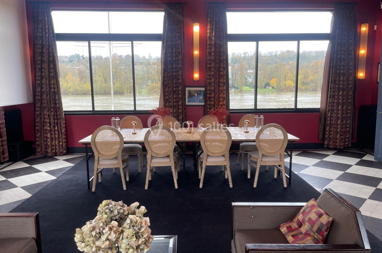 Salle de réunion lumineuse avec une grande table, des chaises en bois clair et des fenêtres donnant sur un paysage automnal.