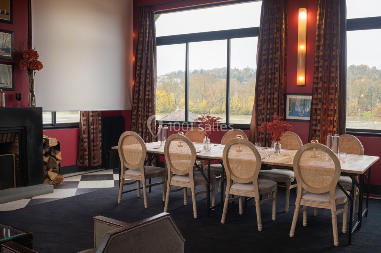 Salle de réunion lumineuse avec une grande table, des chaises en bois clair, des fenêtres donnant sur un paysage automnal.