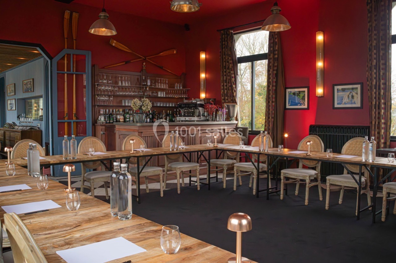 Salle de réunion lumineuse avec tables en bois disposées en U, chaises en rotin et décorations murales rouges.