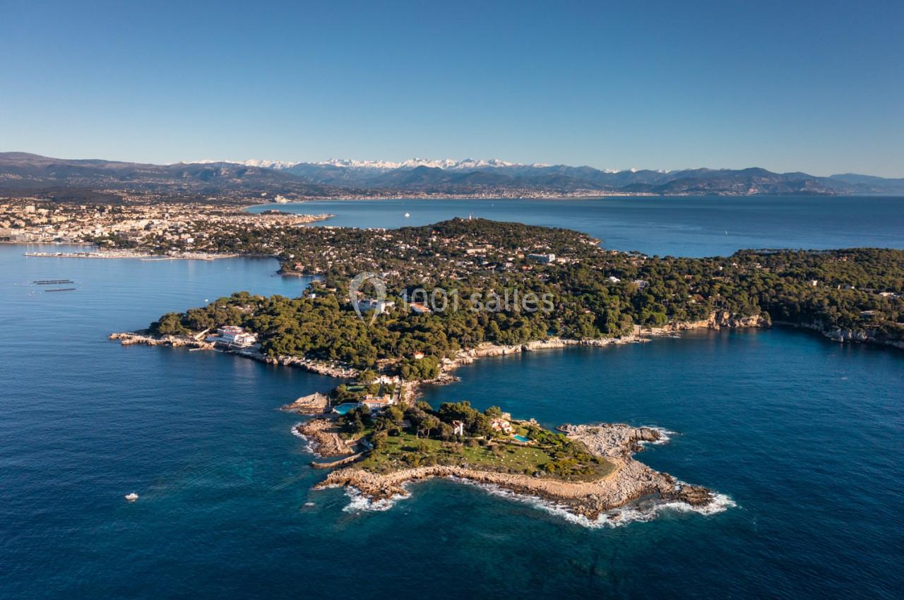Vue aérienne d'une péninsule boisée entourée de mer, avec des montagnes enneigées à l'horizon.