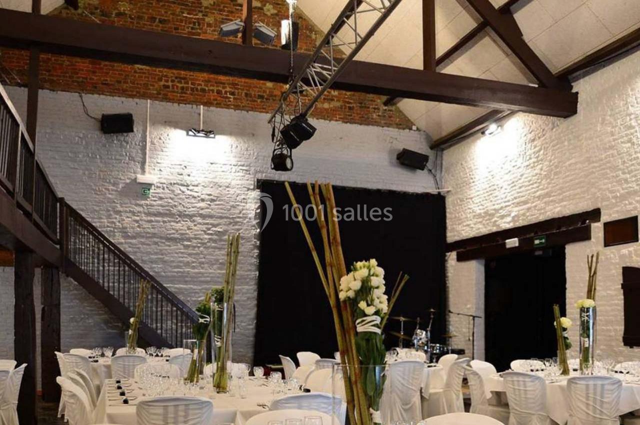 Salle de réception avec murs en briques, plafond en poutres apparentes, tables dressées et décorations florales.