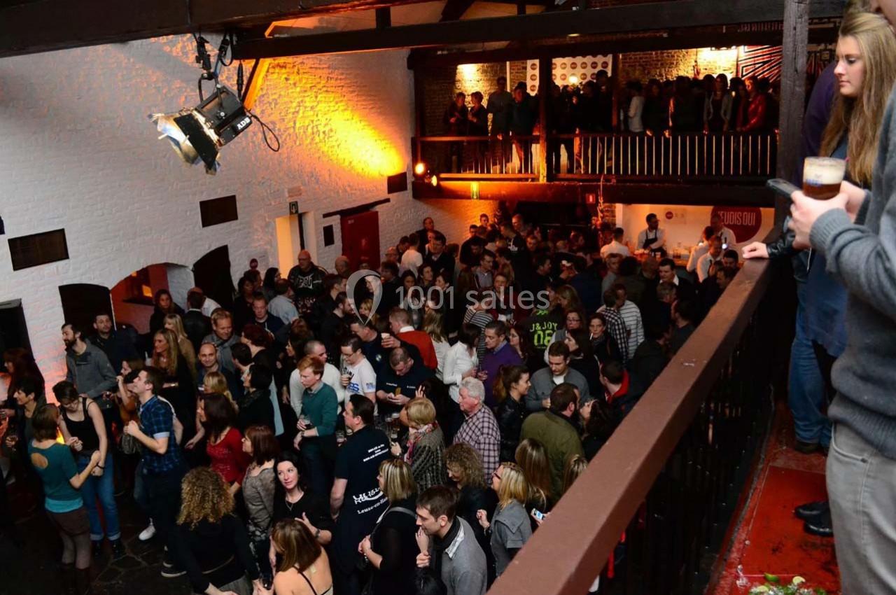 Foule rassemblée dans une salle avec mezzanine, éclairée par des lumières chaudes, lors d'un événement festif.