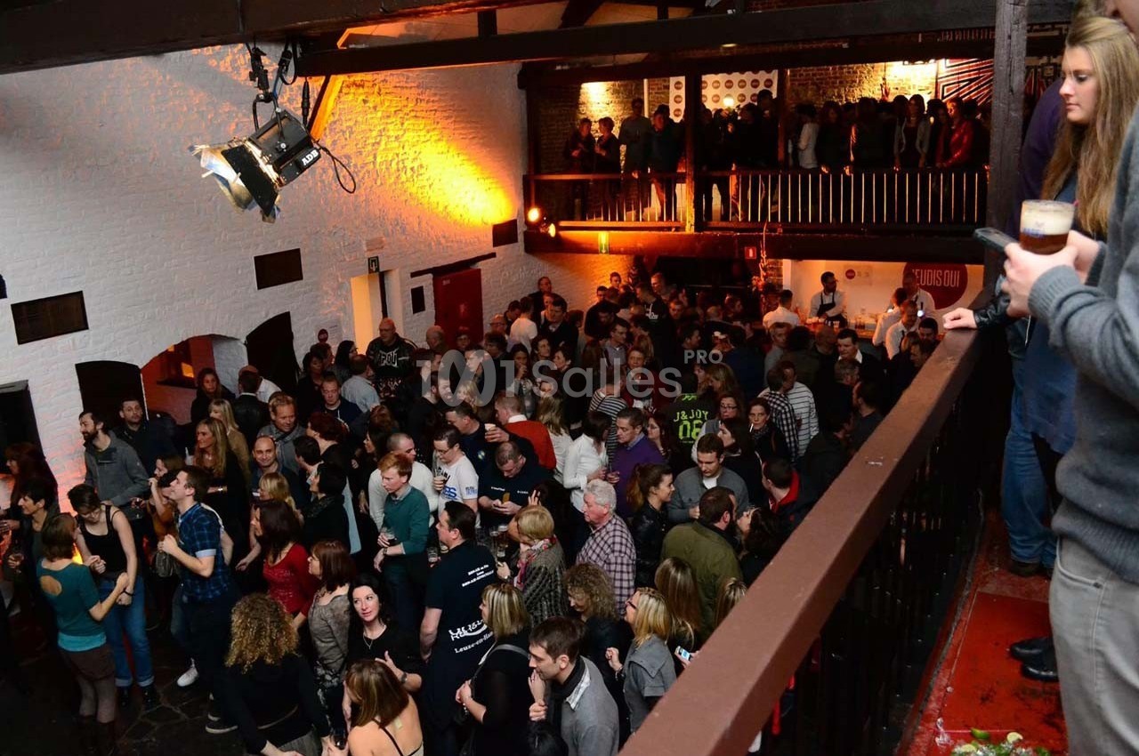 Foule rassemblée dans une salle avec mezzanine, éclairée par des lumières chaudes, ambiance festive.