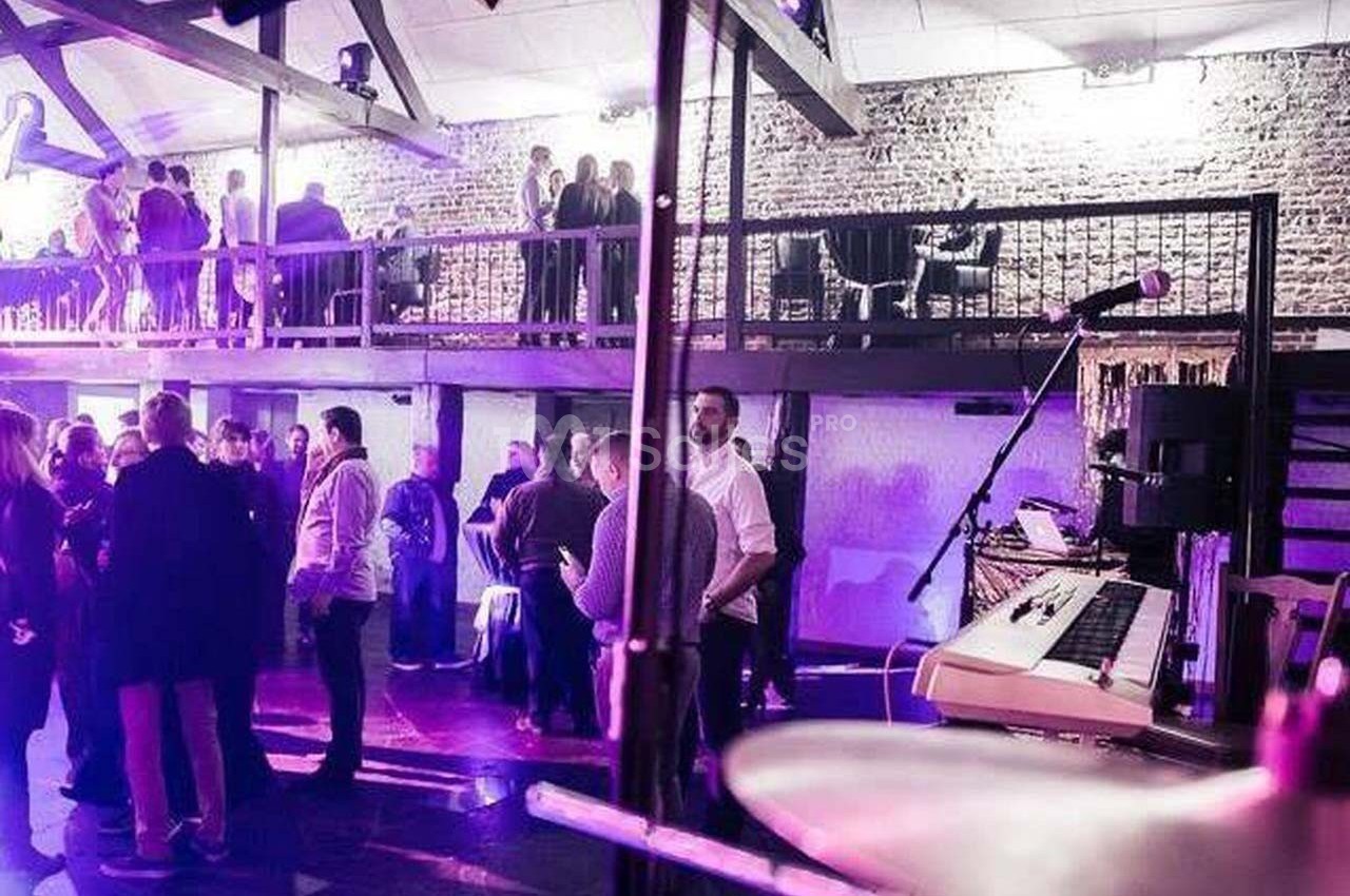 Groupe de personnes discutant dans une salle avec mezzanine, éclairage violet et instruments de musique au premier plan.