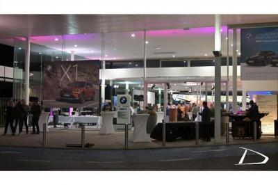 Vue nocturne d'un showroom automobile éclairé, avec une affiche promotionnelle d'un véhicule BMW X1 au premier plan.