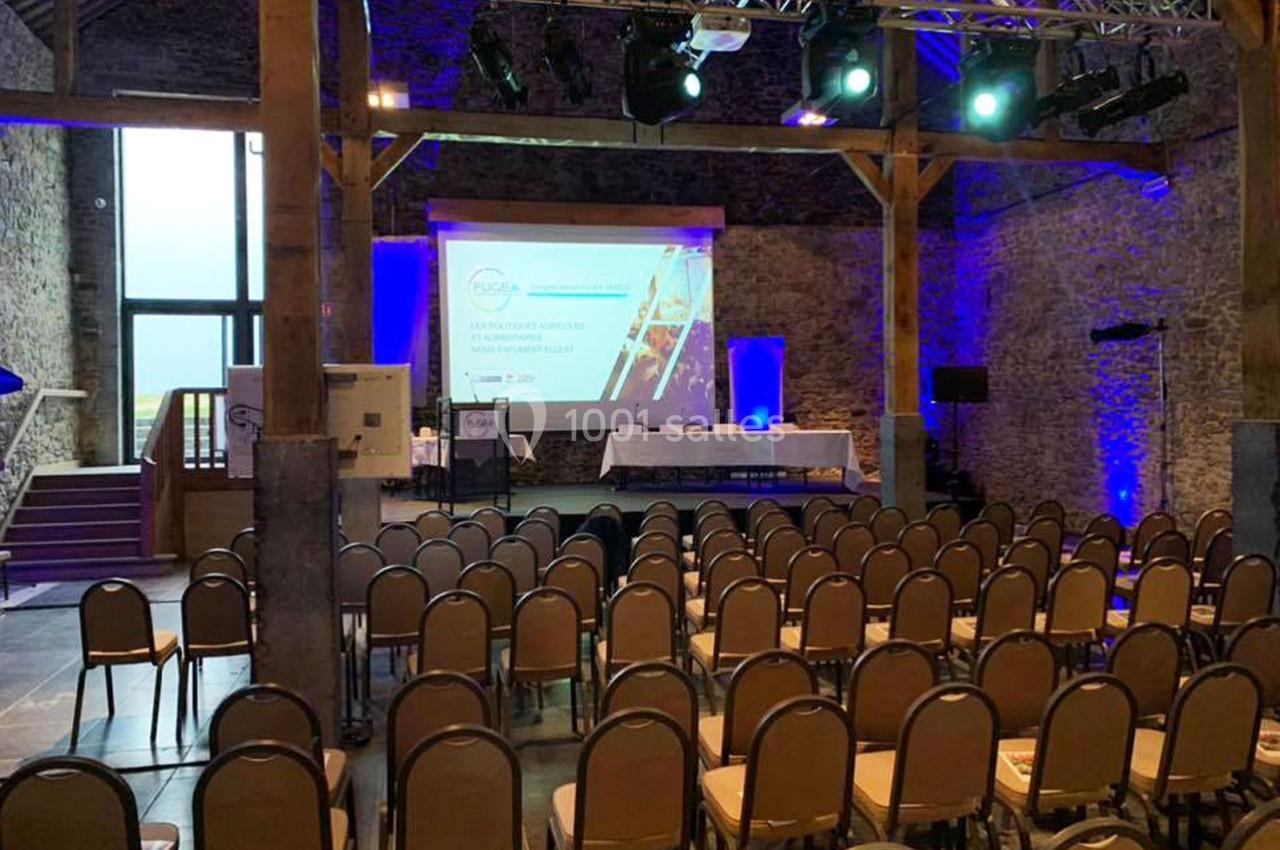 Salle de conférence avec des rangées de chaises vides, un écran de projection allumé et un éclairage coloré.