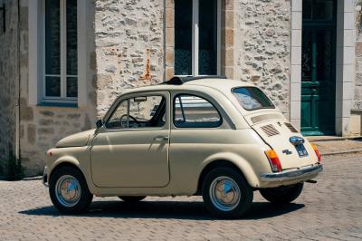 Voiture ancienne décapotable rouge garée sur une pelouse, entourée d'arbres en arrière-plan.