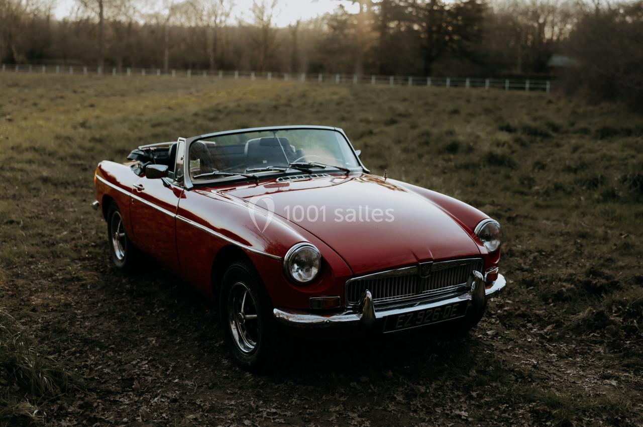 Voiture décapotable rouge ancienne stationnée dans un champ au coucher du soleil.