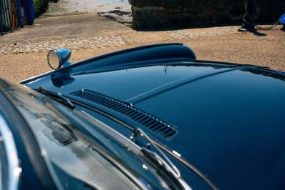 Roue avant d'une voiture vintage beige avec un enjoliveur chromé, stationnée sur un sol gravillonné.