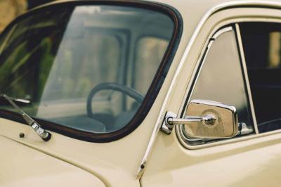 Roue avant d'une voiture vintage beige avec un enjoliveur chromé, stationnée sur un sol gravillonné.