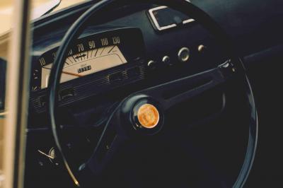 Roue avant d'une voiture vintage beige avec un enjoliveur chromé, stationnée sur un sol gravillonné.