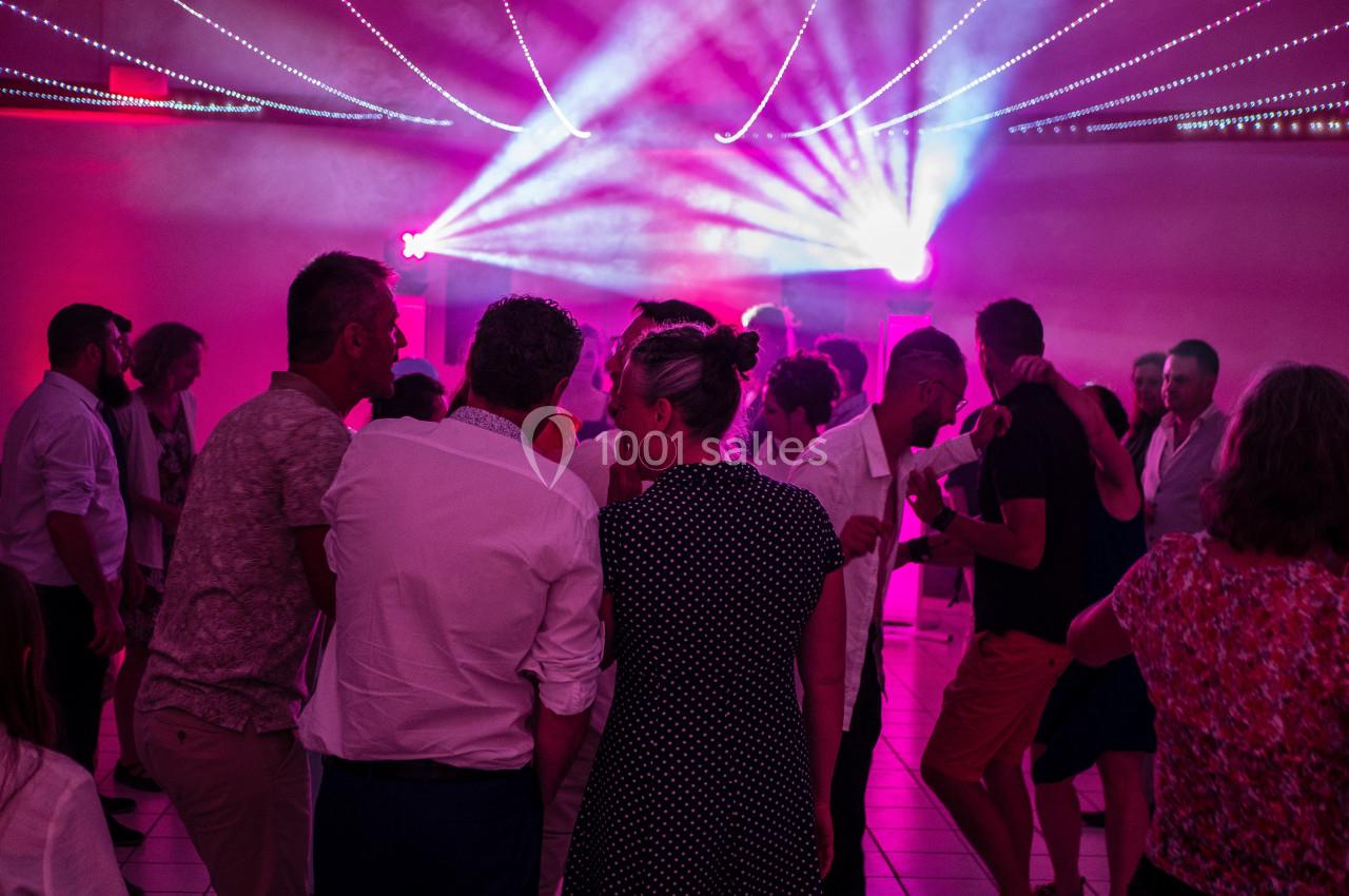 Groupe de personnes dansant sous des lumières colorées dans une ambiance festive en intérieur.