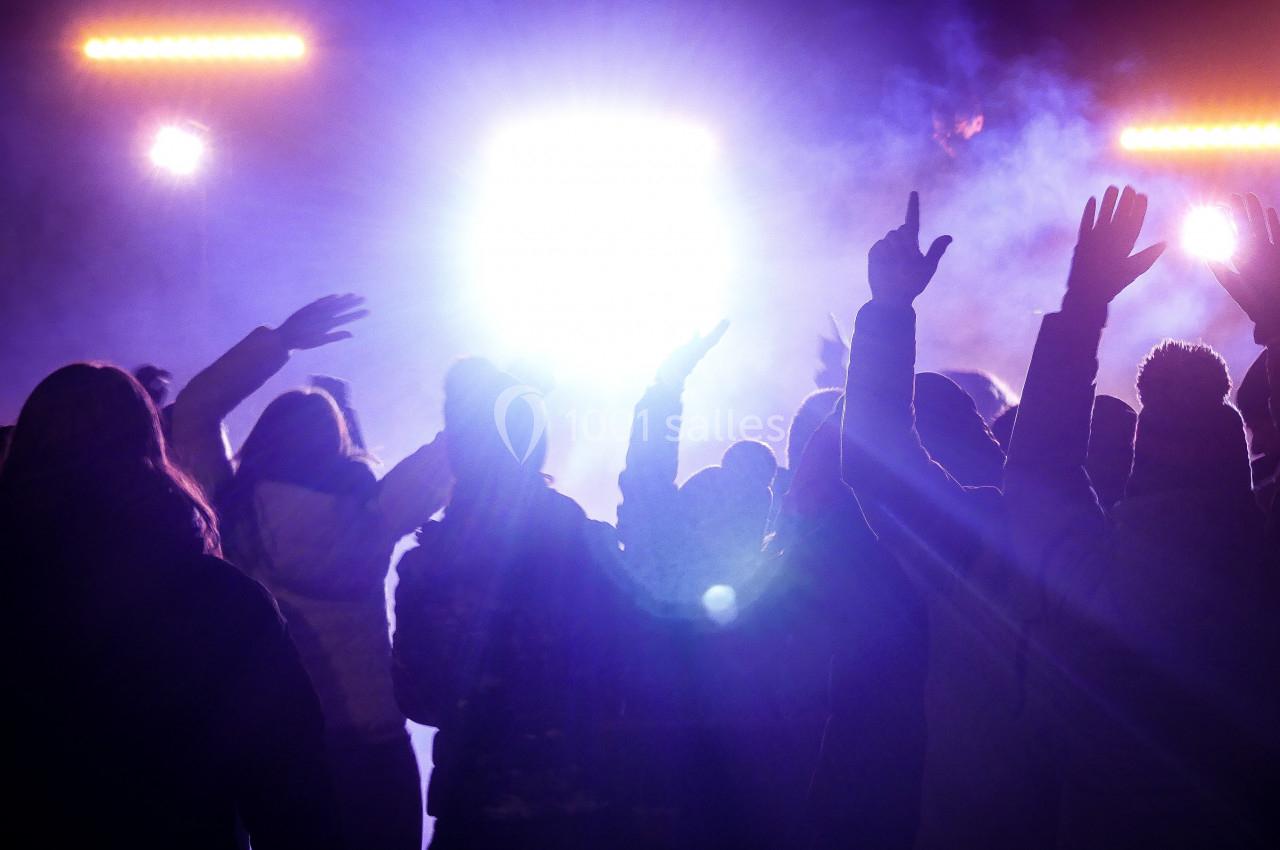Groupe de personnes levant les bras lors d'un concert ou d'un événement avec des lumières vives en arrière-plan.