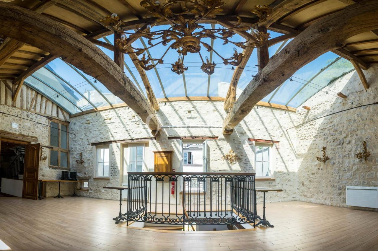 Plafond en verre sous charpente apparente dans une pièce lumineuse aux murs en pierre et parquet au sol.