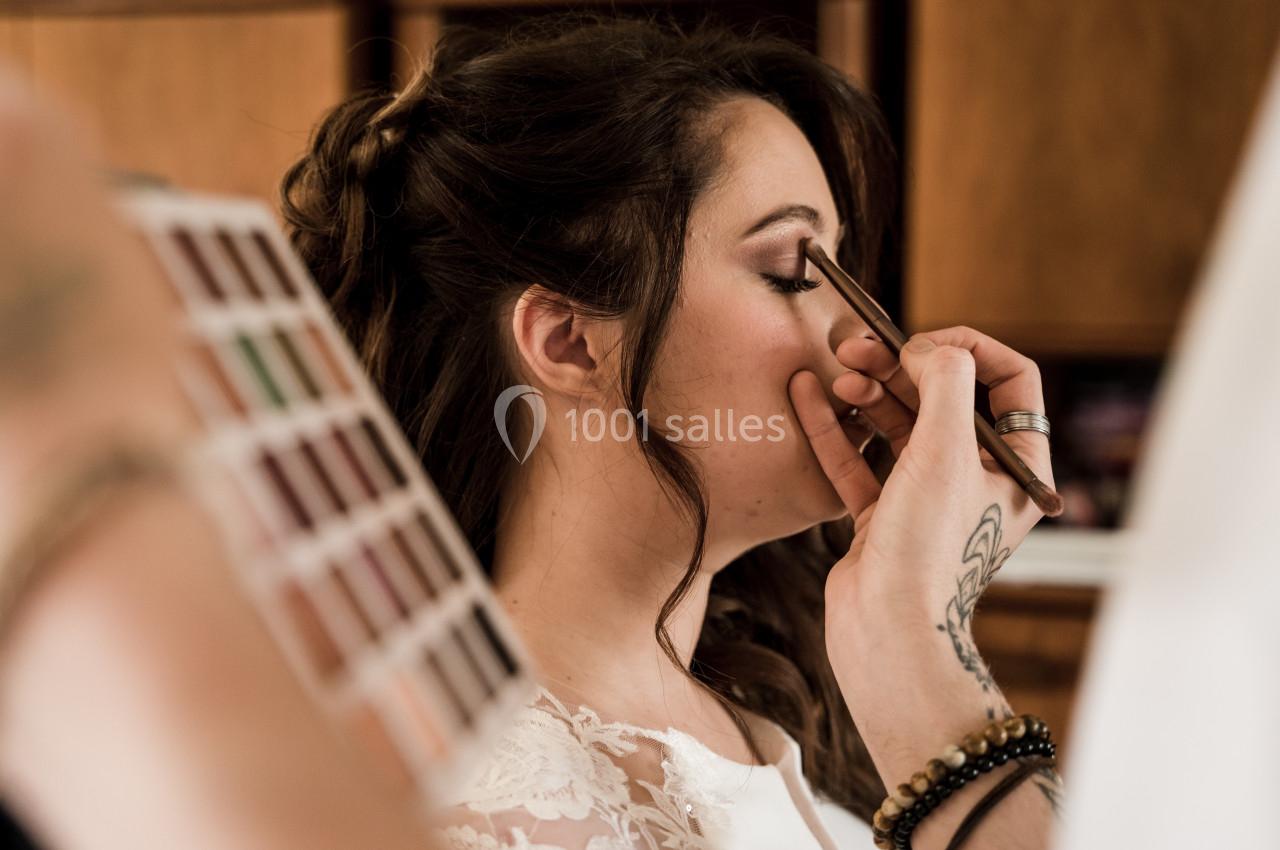 Une maquilleuse applique du fard à paupières sur une femme aux cheveux bruns dans un cadre intérieur.